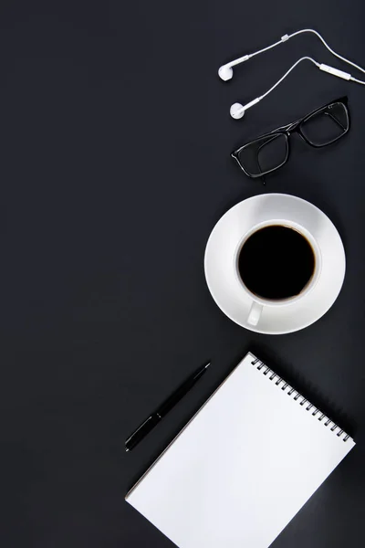 Scrivania nera per ufficio con penna per notebook, occhiali, cuffie e una tazza di caffè. — Foto Stock
