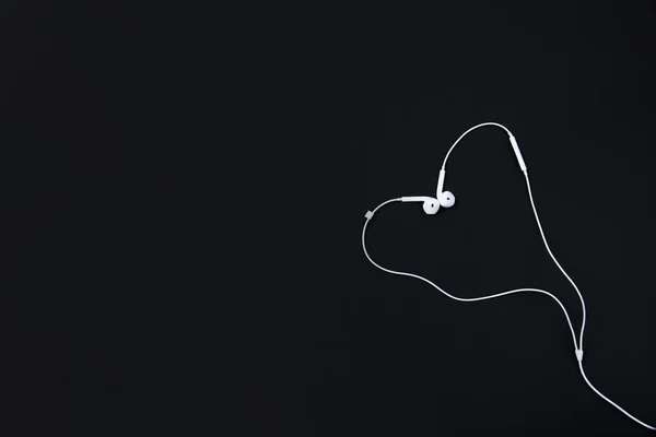 Bílá sluchátka leží na černém pozadí ve tvaru srdce. — Stock fotografie