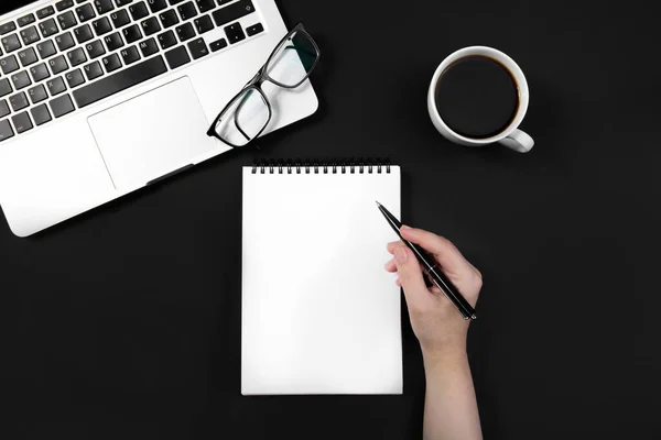 Hand holds pen over notebook on black table near laptop. — Stock Photo, Image