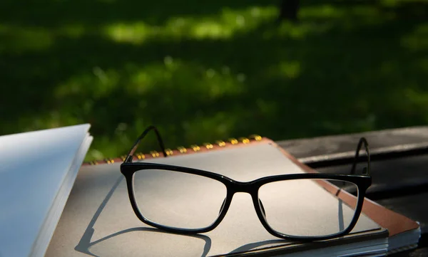 Glasses lie on top of a pile of books with a notebook on a bench in the park — Stock Photo, Image