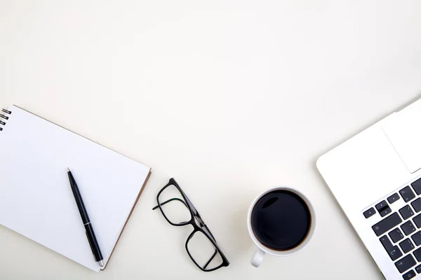 light office desk with laptop, white notebook mockup, glasses and coffee cup.