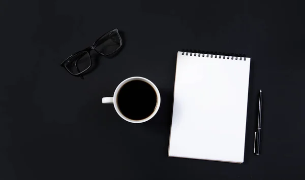 Tazza di caffè, bicchieri e blocco note bianco con penna su sfondo nero. vista dall'alto — Foto Stock