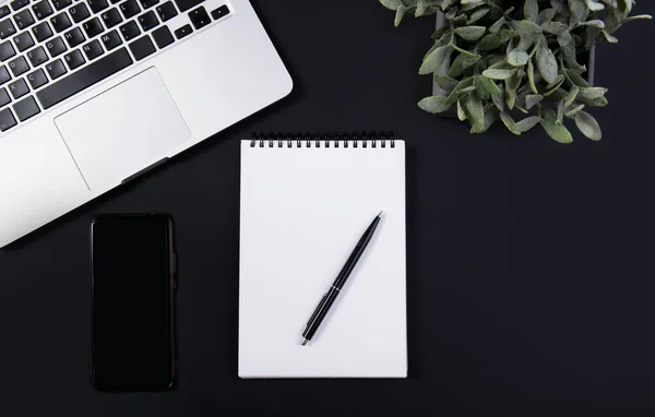 Black office desk with laptop, smartphone, notebook and pen. Top view — Stock Photo, Image