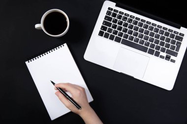  El, dizüstü bilgisayarın yanındaki siyah masada kalemi tutuyor..