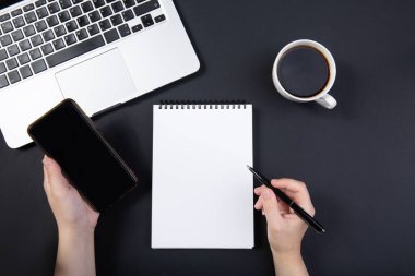  El, dizüstü bilgisayarın yanındaki siyah masada kalemi tutuyor..