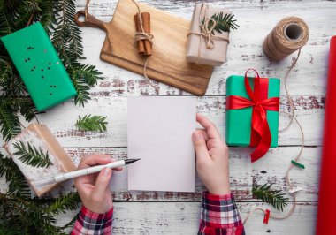 Eller masanın üzerinde hediyelerin yanında bir kalem ve kartpostal tutar.