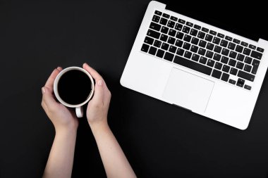  Eller bir fincan kahveyi laptopun yanındaki siyah masada tutar. 