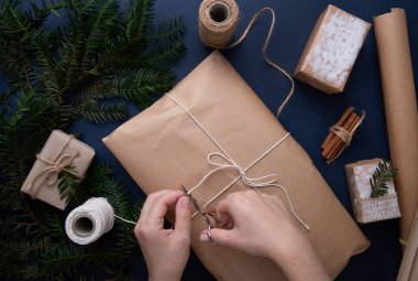  Mavi bir arka planda Noel hediyesi paketleyen eller.