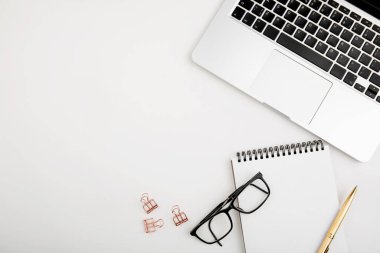 Dizüstü bilgisayarı, beyaz defter modeli, gözlükleri ve altın kalemi olan ofis masası. 