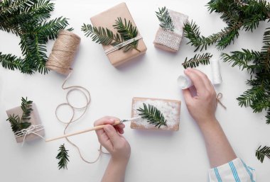 Eller bir Noel hediyesini tutar ve onu beyaz boyayla süsler. 