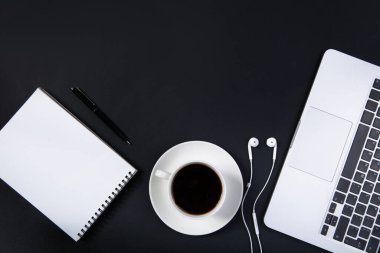 Laptoplu siyah ofis masası, beyaz model defter, kalem ve bir fincan kahve.. 
