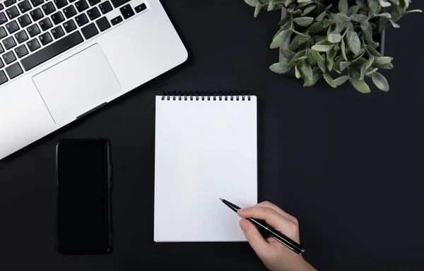 Hand holds pen over notebook on black table near laptop. — Stock Photo, Image