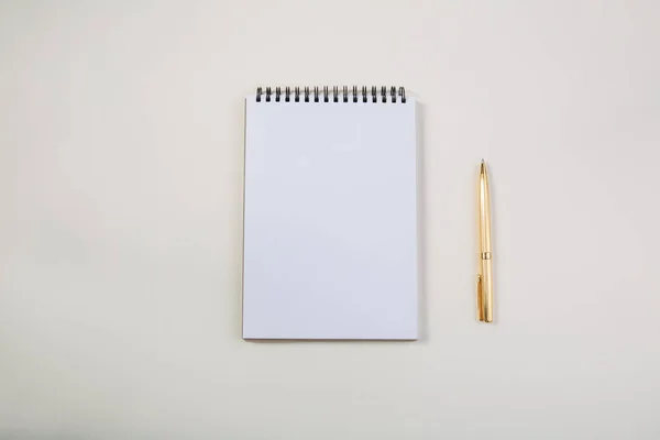 Blocco note bianco con penna dorata su tavolo chiaro, vista dello spazio libero per il testo — Foto Stock