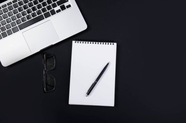 Laptoplu, gözlüklü ve kalemli siyah ofis masası. Üst görünüm 
