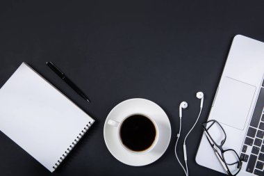 Laptop, akıllı telefon, kalem, bardak ve bir fincan kahveli siyah ofis masası.. 