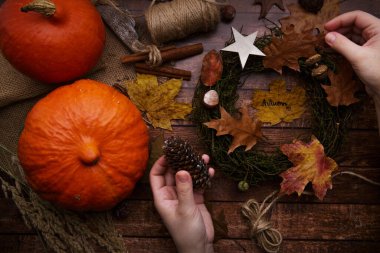 Çocuk elleri bir kozalak tutar ve masanın üzerinde bir sonbahar çelengi bir balkabağı.