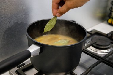  İnsan eli, patates tenceresine bir defne yaprağı ve sobadaki eti ekler.