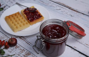 Bir kavanoz çilek reçeli ve beyaz bir masada bir tabak Belçika waffle 'ı.