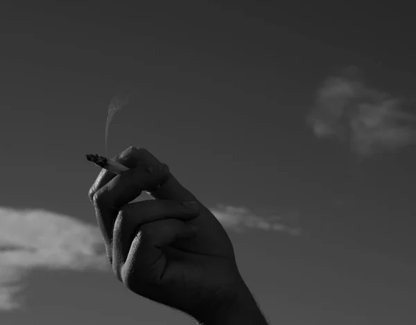 Cigarro na mão de um homem contra um céu azul. de perto. — Fotografia de Stock