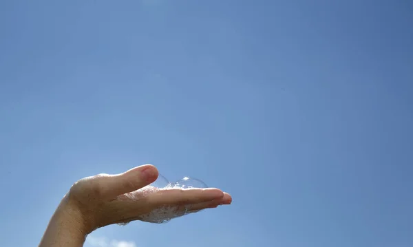 푸른 하늘 배경에 비누 거품이 나는 여성 손바닥을 클로즈업 — 스톡 사진