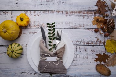Masanın üzerinde sarı yapraklar, çatal bıçaklar ve balkabakları var.