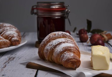 Kruvasan çilek reçeli ve tereyağı ahşap bir masanın üzerinde.