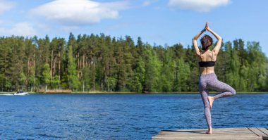Yoga pozisyonunda, gölde yoga yapan bir kadın. Doğa arka planında fitness yaşam tarzı. Güneşli bir gün. Boşluğu kopyala 