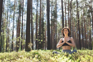 Ormanda yoga yapan bir kadın ve arkasında namaste var. Doğa arka planında fitness yaşam tarzı. Çam ormanında güneşli bir gün. Boşluğu kopyala