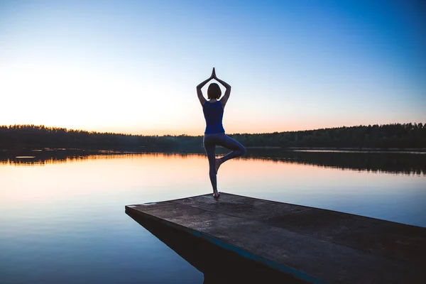 Mulher praticando ioga em um lago de pé no log em pose de árvore de ioga. estilo de vida fitness ao ar livre natureza fundo. Pôr do sol no lago. espaço de cópia — Fotografia de Stock