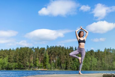 Yoga pozisyonunda, gölde yoga yapan bir kadın. Doğa arka planında fitness yaşam tarzı. Güneşli bir gün. Boşluğu kopyala 