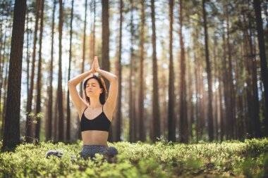 Kafasında namaste olan bir kadın ormanda yoga yapıyor. Doğa arka planında fitness yaşam tarzı. Çam ormanında güneşli bir gün. Boşluğu kopyala
