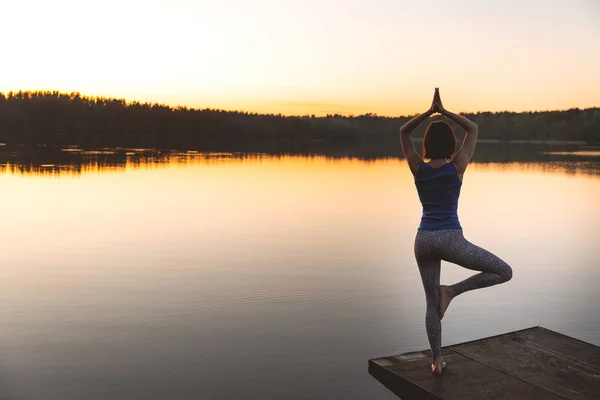 Mulher praticando ioga em um lago de pé no log em pose de árvore de ioga. estilo de vida fitness ao ar livre natureza fundo. Pôr do sol no lago. espaço de cópia — Fotografia de Stock