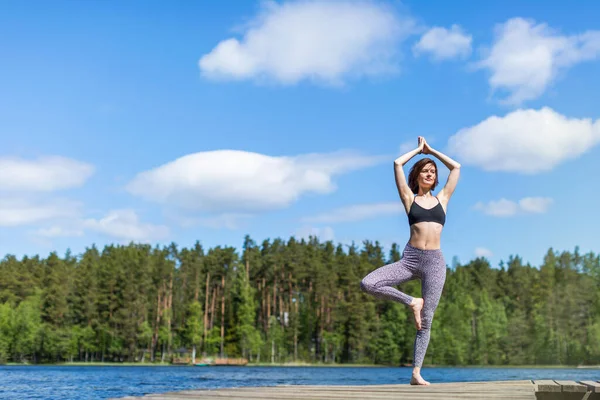 Yoga pozisyonunda, gölde yoga yapan bir kadın. Doğa arka planında fitness yaşam tarzı. Güneşli bir gün. Boşluğu kopyala 