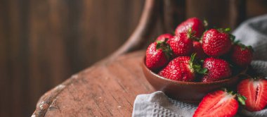 Eski ahşap masadaki kasede taze çilekler. Kapat. Pankart