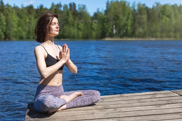 Arkasından namaste ile yoga yapan bir kadın. Açık deniz arka planında fitness yaşam tarzı. Çam ormanında güneşli bir gün. Boşluğu kopyala