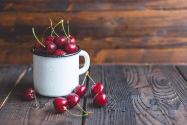 Taze kırmızı, olgun, organik, tatlı kirazlı, ahşap arka planda beyaz bir fincanda su damlaları. Metin için boşluk. Yakın çekim