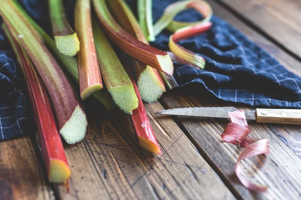Taze organik bahçe rhubarb 'ı ahşap zemin üzerinde bıçak ile saplanır. Koyu yiyecek konsepti. Yaz limonatası, reçel ya da pasta malzemeleri.