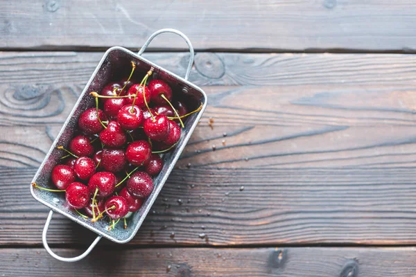 Fresh red ripe organic macro sweet cherry with waterd drops in metal basket on wooden background. space for text. closeup. top view