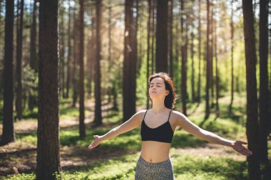Yüksek ağaçlara ve çam ormanlarına karşı elleri açık mutlu bir kadın. Yoga çalışmasından sonra doğanın tadını çıkar. Özgürlük ve hayal gücü kavramı