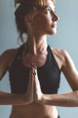 Yoga yapan kadın namaste pozu veriyor, gri duvar arkası, seçici odaklanma. Boşluğu kopyala.