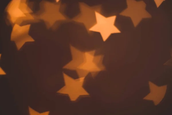 Odaklanamayan soyut Bokeh ışıkları koyu arkaplanda noel yıldızı şeklinde. turuncu, altın ve kahverengi renkler. Noel ve yeni yıl konsepti