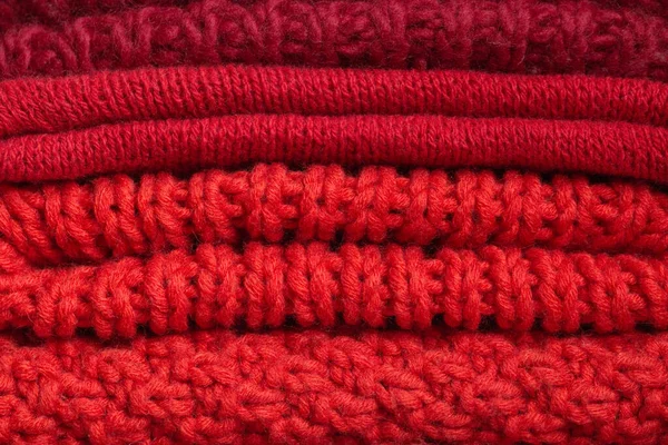 Pile of knitted woolen sweaters red colors. Clothes with different knitting patterns folded in stack. Warm cozy winter and fall knitwear concept. christmas time.close up — Stock Photo, Image