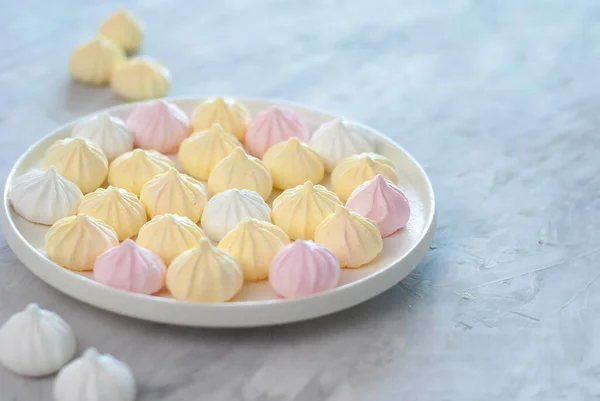 Detailní drobné meringues růžové, bílé a žluté barvy v bílé míse nad bílým světle šedý stůl. Sladký dezert — Stock fotografie