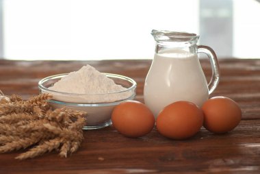 Süt, buğday unu ve yumurtalar koyu kahverengi ahşap arka planda doğal renklerde.