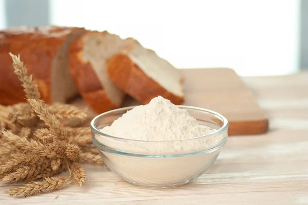 Glass bowl with flour and branches of natural wheat on the light white wooden table and bread pieces — Stock Photo, Image