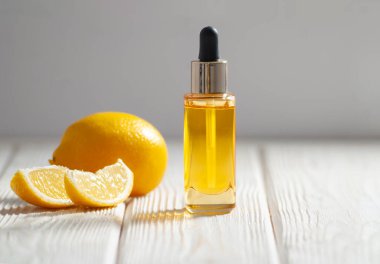 Sarı kozmetik yağı ve hafif ahşap üzerine dilimlenmiş limon parçaları ve yakın plan gri arkaplan resmi. Meyve asidi konseptli doğal kozmetikler