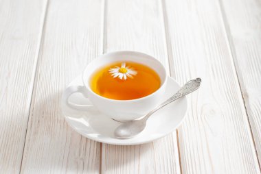 Beyaz ahşap arka planda papatya çiçekli bir fincan bitki çayı. Doğal organik alternatif tıp