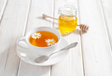 Beyaz bir fincan papatya çiçekli bitki çayı ve beyaz ahşap arka planda bal. Doğal alternatif tıp