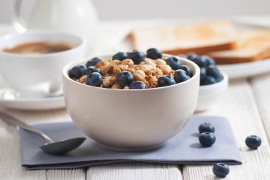Granola ve yaban mersinli kahvaltı, portakal suyu tostlu süt beyaz ahşap masada yakın plan. Sabahları sağlıklı ve lezzetli yiyecekler, fındıklı yulaf ezmesi ve meyveli böğürtlen.