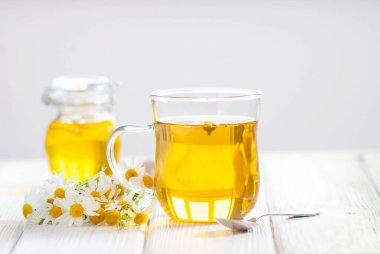 Papatya çiçekli bir fincan bitki çayı ve beyaz ahşap arka planda bal. Doğal organik alternatif tıp kavramı. Yakın çekim.